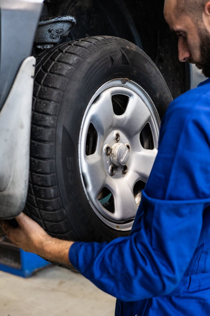 our-story A mechanic in blue uniform closely examines a car wheel for repairs.
